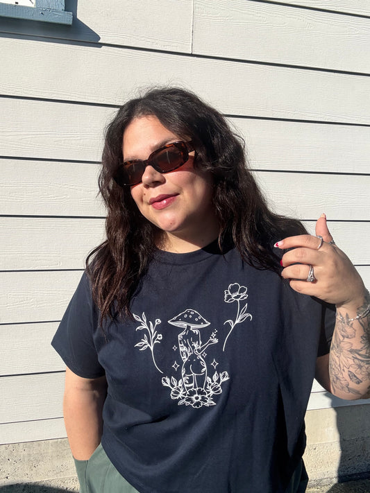 Person wearing a black t-shirt with a white floral design on a wooden floor.
