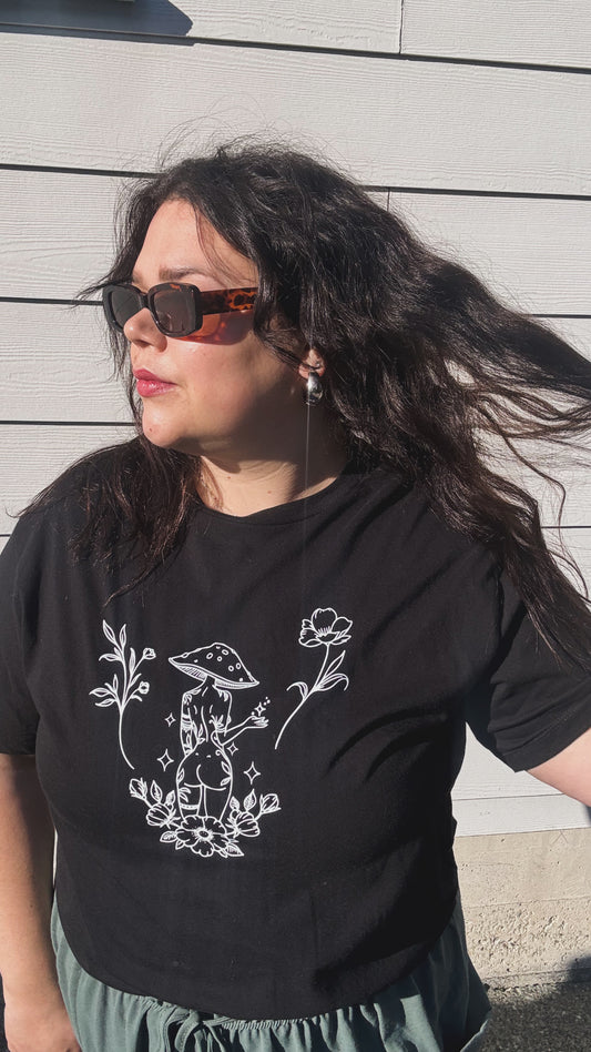 Person wearing a black t-shirt with a white graphic design against a light wooden panel background